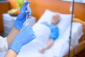 Healthcare worker prepares syringe as elderly patient rests.