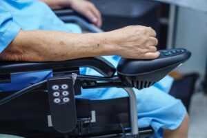 Elderly old lady woman patient on electric wheelchair with remote control at nursing home.