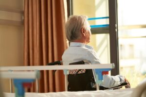 Rear view of senior man sitting in wheel chair in nusing home looking out of window