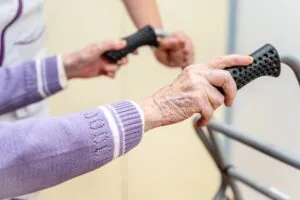 Close-up of an elderly resident holding a walker under staff supervision in an assisted-living facility.