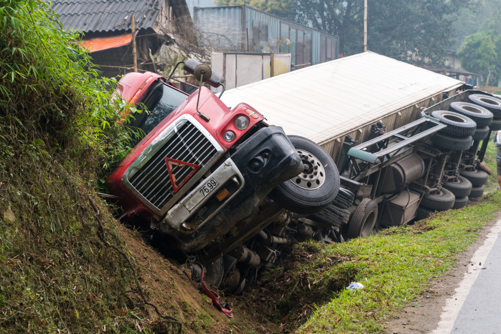 A semi-truck lying overturned in a roadside ditch after an accident.