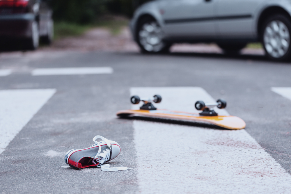 A skateboard and a single shoe lying in a crosswalk near a stopped car.