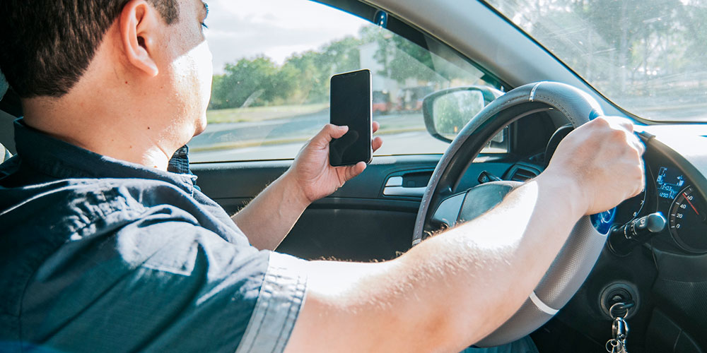 Driver holding a cell phone while steering a moving car, representing distracted and reckless driving behavior that can support punitive damage claims in South Carolina.
