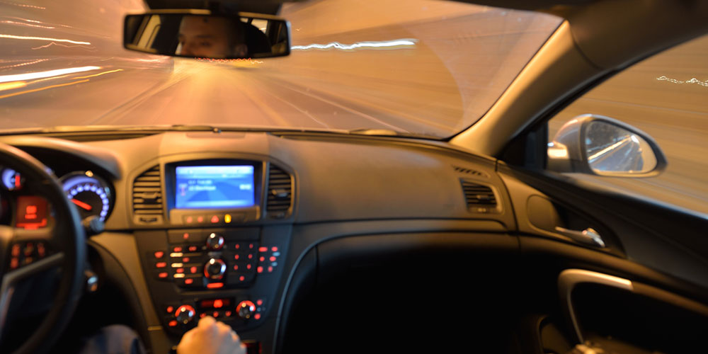 Car driving at night on a dark roadway, representing high-speed driving and dangerous conditions that can elevate a crash from negligence to reckless conduct.