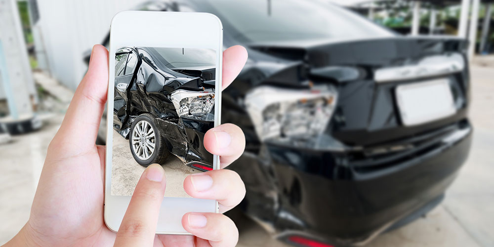 Driver using a smartphone to photograph crash damage at the scene, representing the need to document scrape patterns, debris placement, and vehicle positions after a South Carolina sideswipe accident.