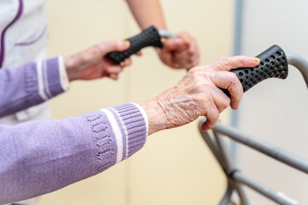 Close-up of an elderly resident holding a walker under staff supervision in an assisted-living facility.